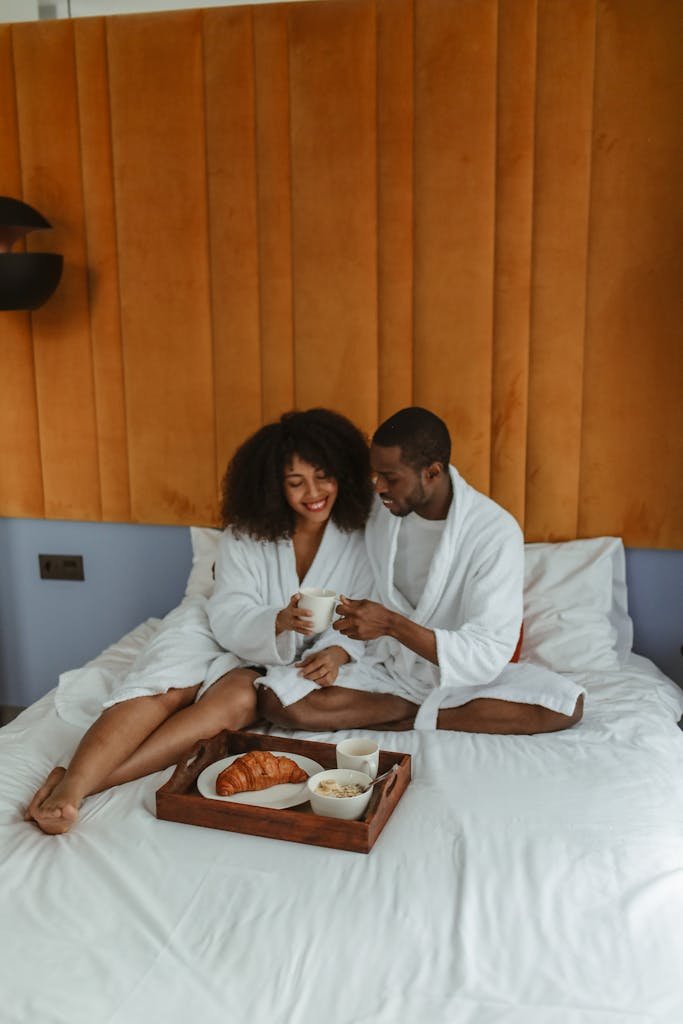 Man and Woman in White Robe Sitting on Bed